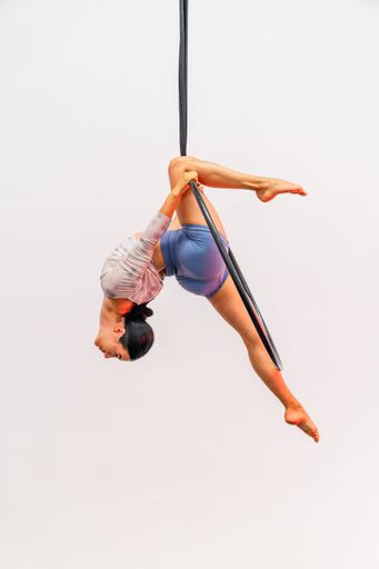 Aerialist woman performs acrobatics on a hoop with a white backdrop