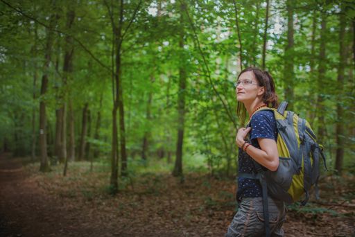 A young woman with a backpack on her back enjoys a hike in the forest.