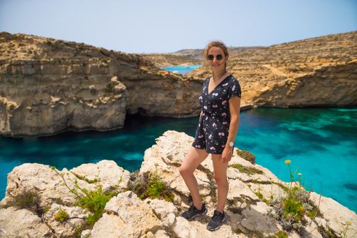 A French woman standing on the stone in Comino Island with calm blue waters in Malta on a sunny day