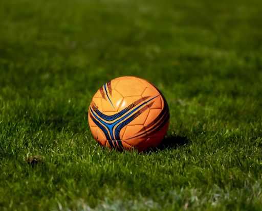 A close-up shot of an orange soccer ball on a green grass field