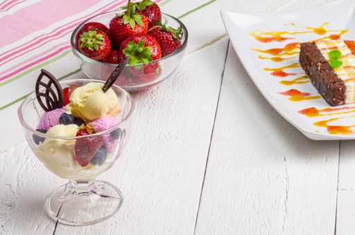 A close up of Ice dessert and dish of strawberries on the table with white planks