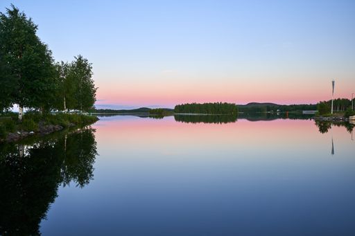 A serene lake reflecting trees and a pastel-colored sky during sunset