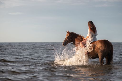 A young woman riding a horse in the sea with splashing water under a clear sky