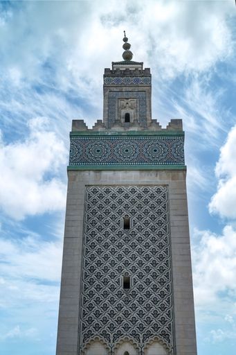 A tall minaret with intricate geometric patterns against a partly cloudy sky.