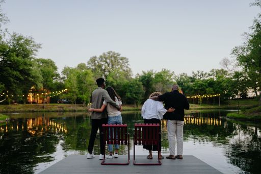 A back shot of two couples standing on a dock by a lake with string lights and trees in the background