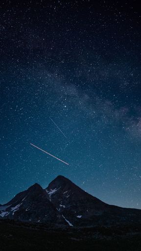 A night sky filled with stars above a mountain range, with visible shooting stars in Italy, Riale