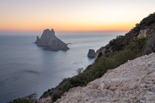 The sunset view of Es Vedra island from a rocky cliff in Ibiza, Spain with a calm sea
