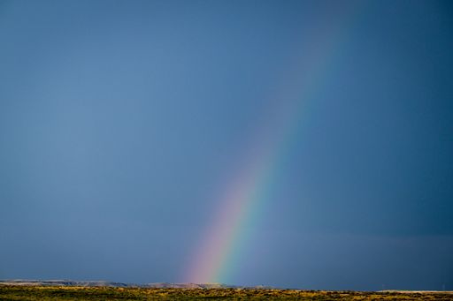 A beautiful rainbow stretching across a clear blue sky over a vast landscape in Cody, Wyoming