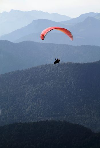 A vertical shot of a person paragliding with an orange parachute over beautiful mountains