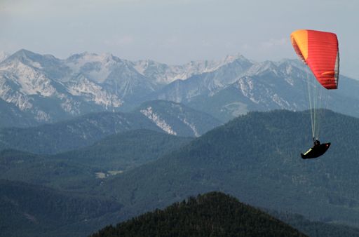 A person paragliding with an orange parachute over beautiful mountains