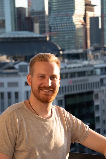 A vertical shot of a Caucasian male in a balcony over the city with high buildings