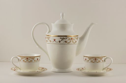 A closeup of elegant white ceramic teacups and a pot with golden decorations on an isolated background