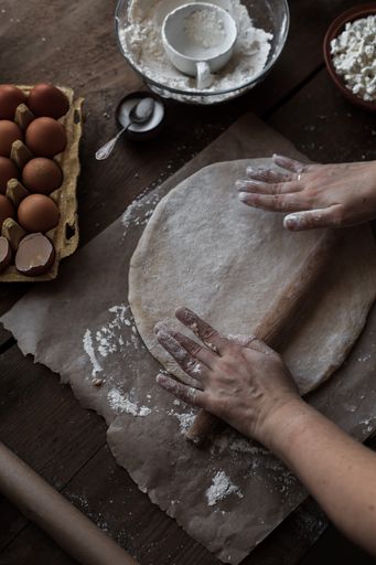 A vertical shot of female hands rolling dough with the board on kitchen table