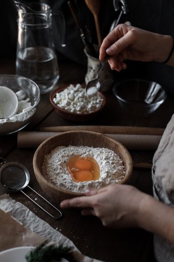 A vertical shot of female hands adding eggs to dough in a wooden bowl
