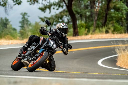A motorcyclist in full gear leaning into a curve on a winding road surrounded by trees