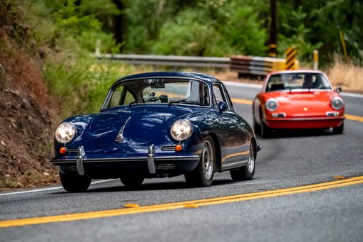 Colorful Vintage cars driving on a winding road through a forested area