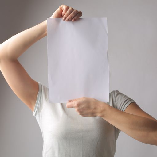 A vertical shot of a woman holding up a sheet of paper with copy space on it in front of her face