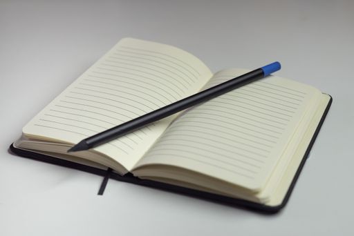 Opened notebook with empty white sheets with horizontal lines and a pencil with a white background