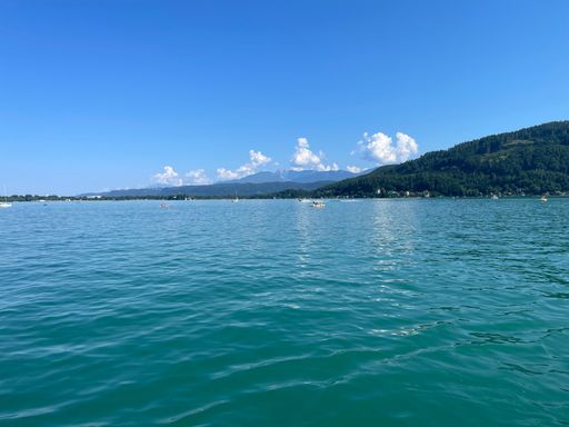 A serene view of a lake with clear blue water and distant mountains under a bright blue sky