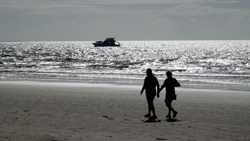 A silhouette of a couple walking on a beach with a boat on the horizon during sunset