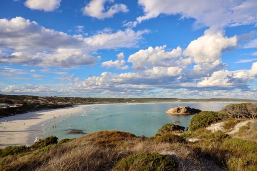 A scenic view of a beach with clear water and a rocky outcrop under a partly cloudy sky