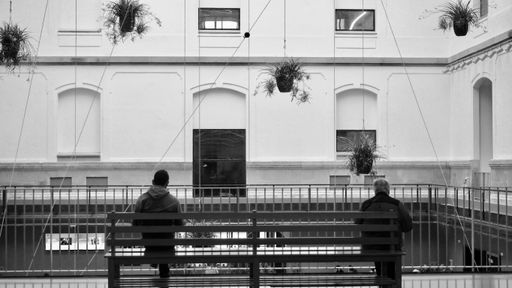 A grayscale shot of two people sitting on the opposite sides of a bench inside of a building