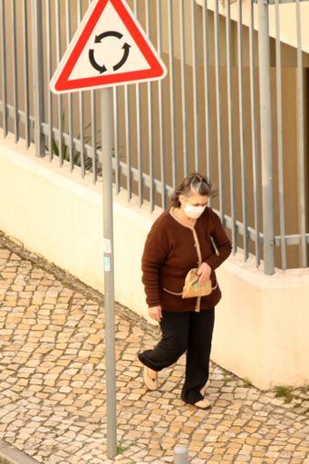A vertical picture of a woman with a face mask walking through the sidewalk - COVID-19 concept