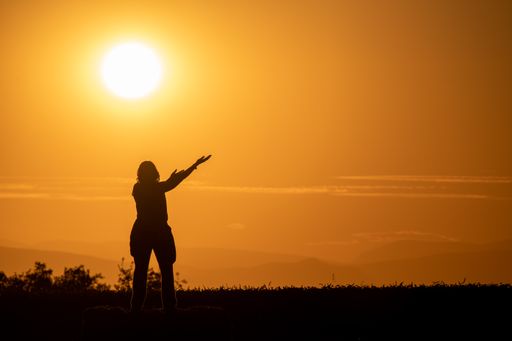 A silhouette of a Caucasian woman in a field with her arms outs in stretched during sunset