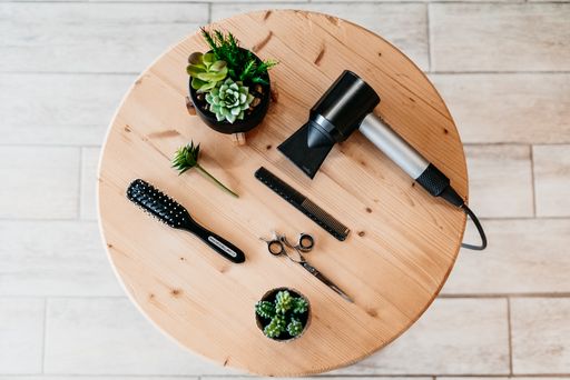 An overhead shot of artificial cactus flowers with scissors, comb and dryer on a round table