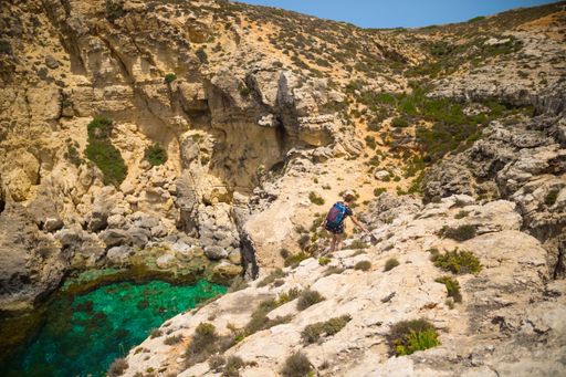 A woman with a backpack hiking in the rocky hills in the Comino Island, Malta