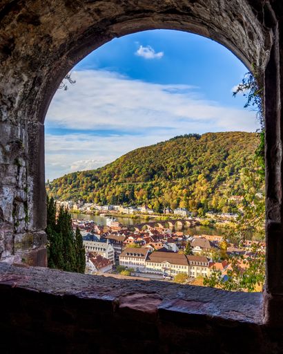 A scenic view of Heidelberg city seen from a stone arch window, with the Neckar River in the background