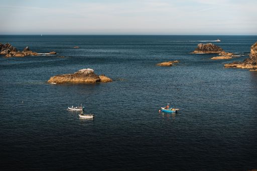 Scenic view of small fishing boats floating on calm sea near rocky coastline under clear sky
