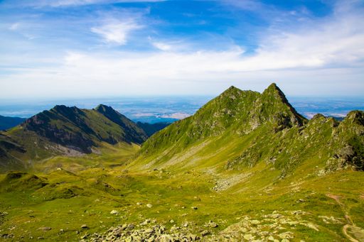 An aerial view of the Fagaras Mountains in Romania with clear blue sky and lush green valleys