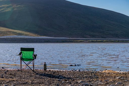 A camping area on a lake in mountainous terrain. A camp chair and a tea thermos on the lakeshore
