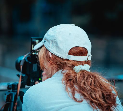 A young woman with red hair and a white cap taking a photograph with a camera on a tripod
