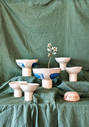 Artistic arrangement of ceramic flower holders with dried flowers on a green fabric background