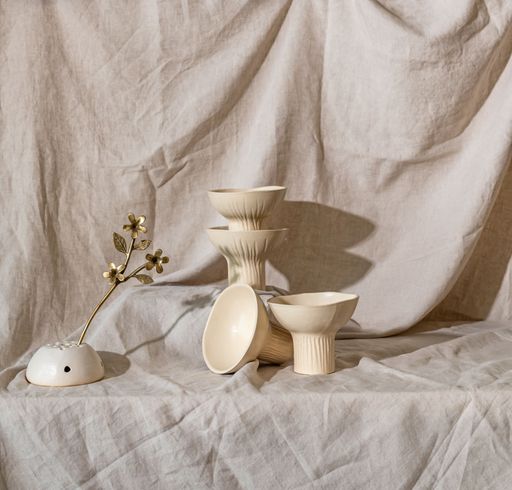 A still life arrangement of beige ceramic bowls and a decorative gold flower on a linen backdrop