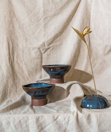 An arrangement of handcrafted ceramic bowls and a decorative golden flower on a beige fabric background