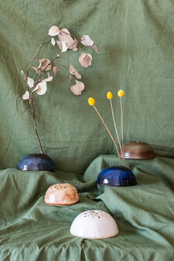 Artistic arrangement of ceramic flower holders with dried flowers on a green fabric background