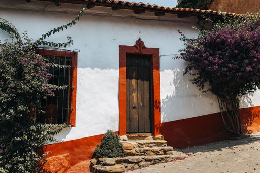 Charming rustic house with white walls and red trim, surrounded by greenery and purple flowers