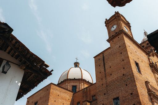 A Low angle view of an old brick church with a clock tower and a dome against a clear blue sky in Mexico