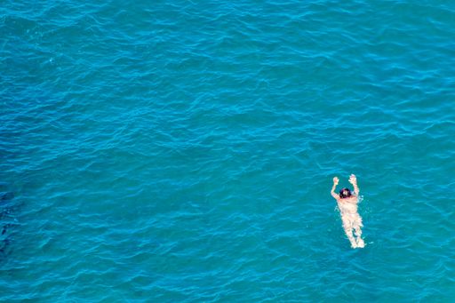 A top view of a man swimming on a deep open sea in summertime