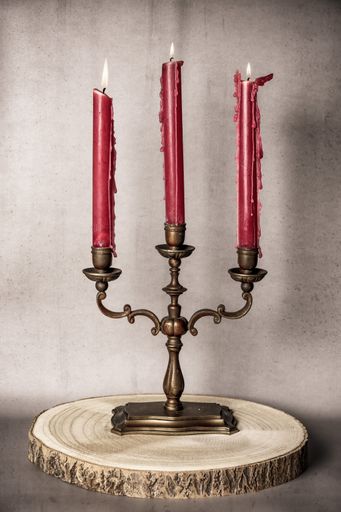 Vintage brass candelabra with three red candles on a wooden slab against a gray background.