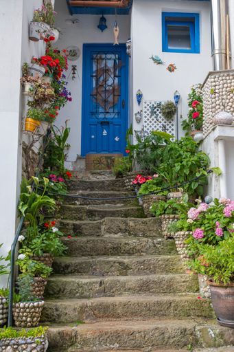 A charming stone staircase adorned with colorful flowers leading to a blue door in Tazones, Span