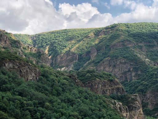 A landscape of rocky hills covered in greenery under a cloudy sky in the countryside