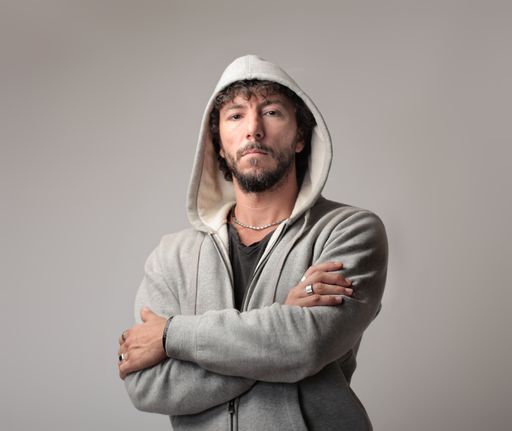 A portrait of a confident Italian man wearing a jacket with a hood and standing with crossed arms