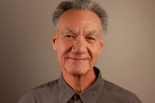 A portrait of a senior Hispanic man smiling against a neutral background