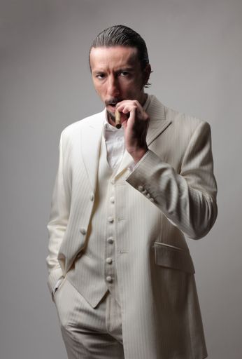 A portrait of an adult Italian mafia boss wearing a white suit and smoking a cigar