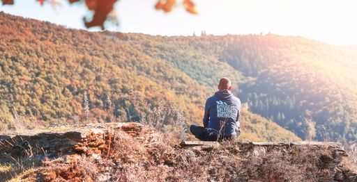 A man sitting on a rocky ledge overlooking a scenic mountain landscape