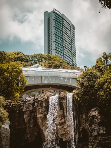 A beautiful tall building in Hong Kong and a waterfall in the park under a cloudy sky, China